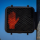 Electronic Don't Walk sign red with hand at cross walk against blue sky with tree in part of background