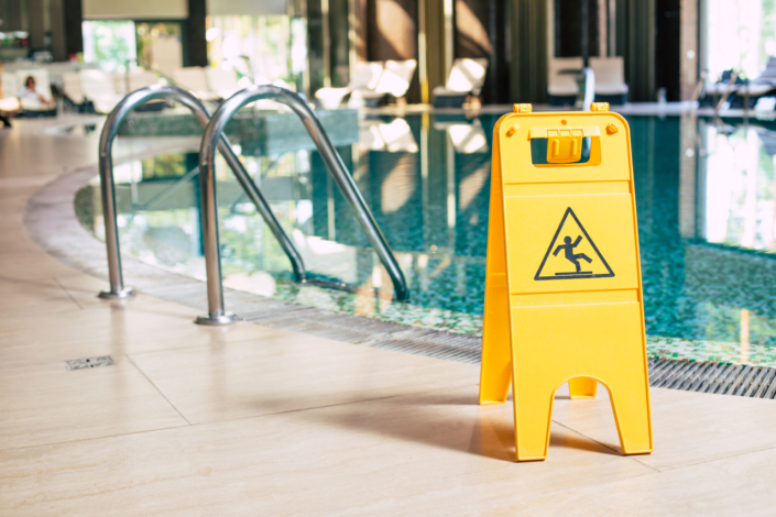 Yellow sign of wet floor plate is near the swimming pool.