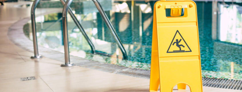 Yellow sign of wet floor plate is near the swimming pool.