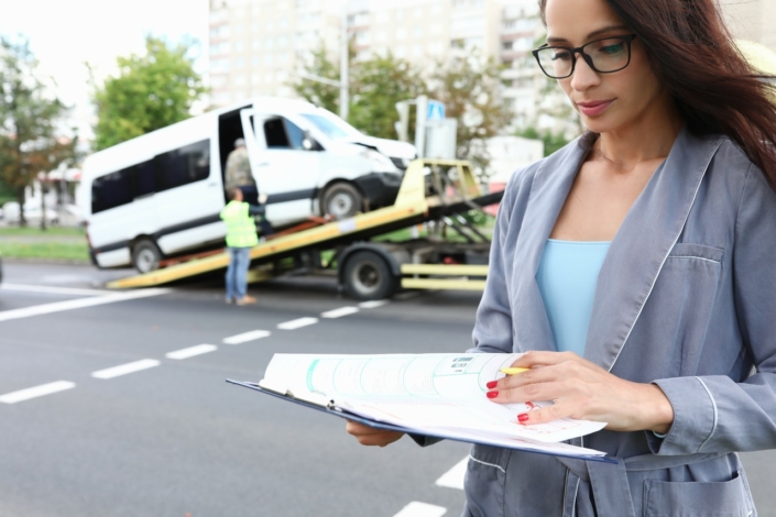 Insurance agent standing near wrecked car on tow truck