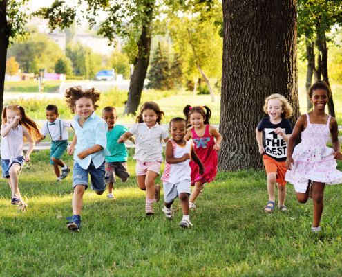 a group of preschoolers running on the grass in the Park.