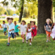 a group of preschoolers running on the grass in the Park.