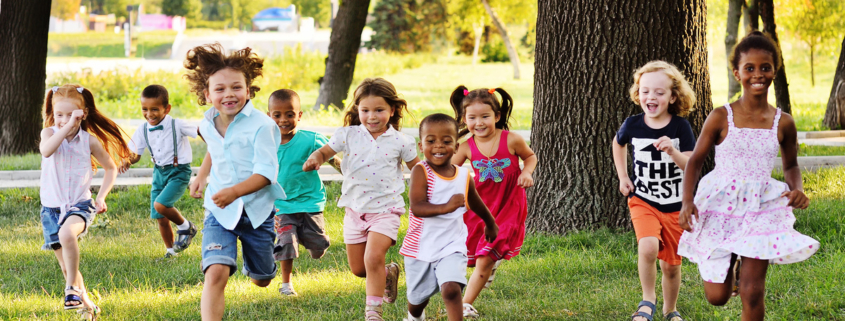 a group of preschoolers running on the grass in the Park.