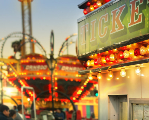 Scene at a classic carnival with rides and focus on ticket booth with subtle retro styling