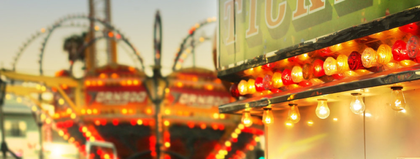 Scene at a classic carnival with rides and focus on ticket booth with subtle retro styling