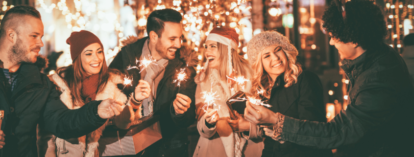 Three couple with sparklers enjoying Christmas outdoor party in the city street at night and with a lot of lights on background.