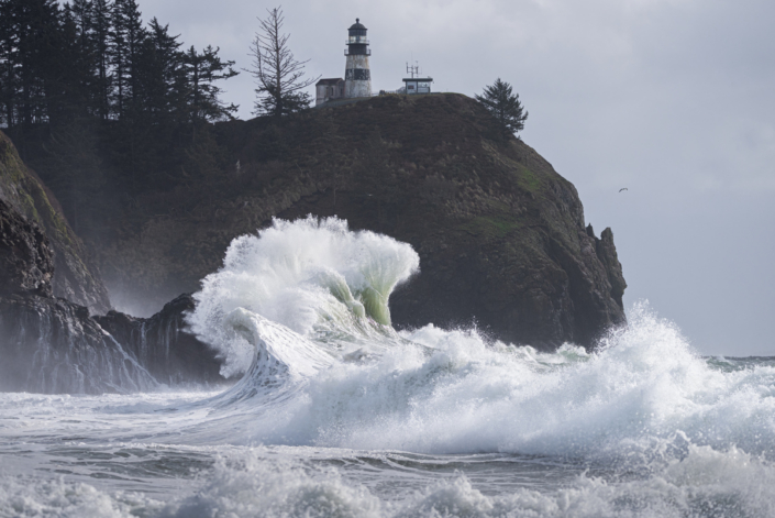 Powerful ocean wave crashing under lighthouse during king tide storms on the Washington coast, Cape Disappointment