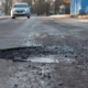 A pothole in the road and a car in the background that is moving towards this pothole
