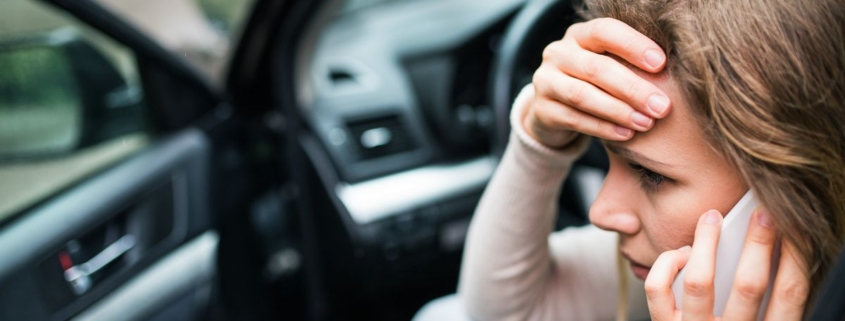 Young woman in the damaged car after a car accident, making a phone call.